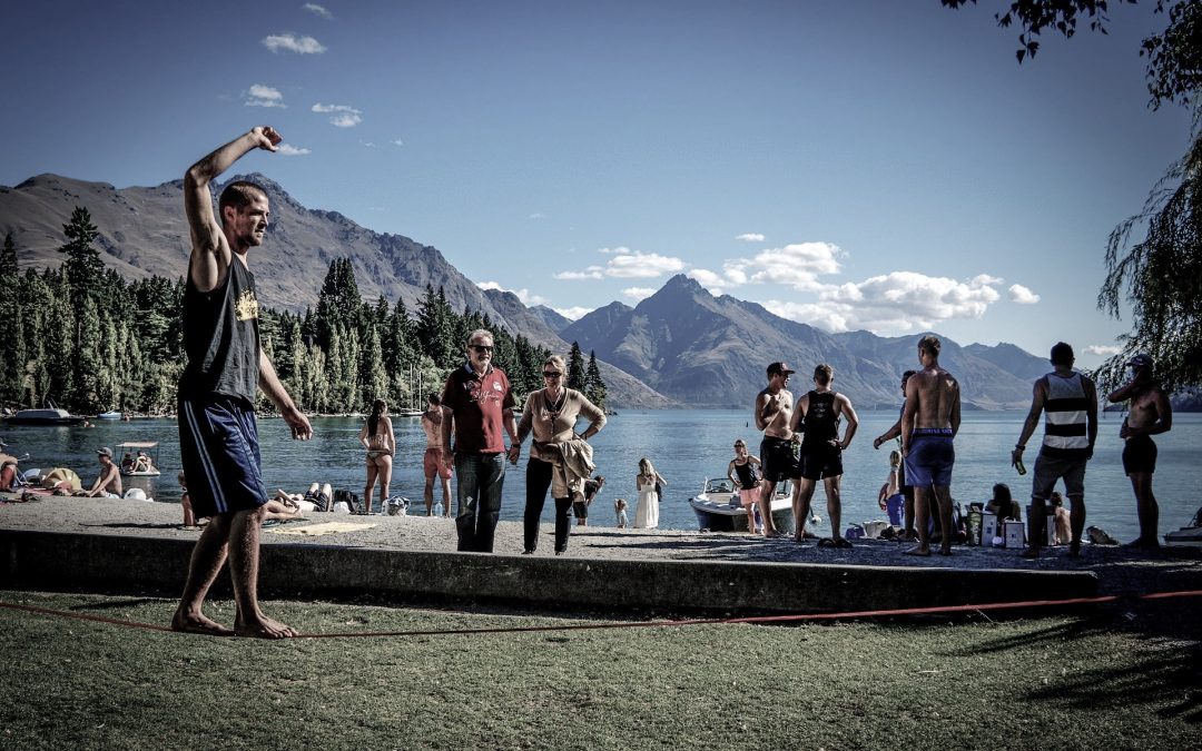Ein Mann balanciert auf einer Slackline vor einem See und einem Berg in der Natur